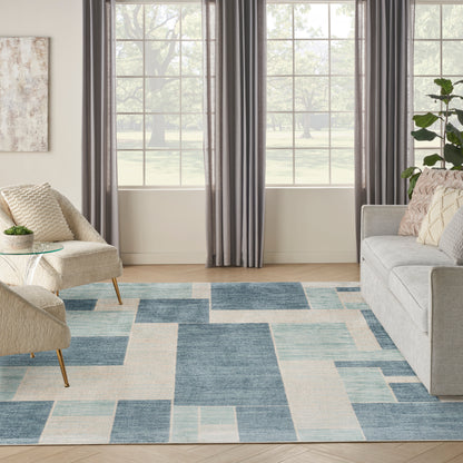 Living room with blue & cream geometric rug, gray sofa, beige armchair, dark curtains, and a potted plant.