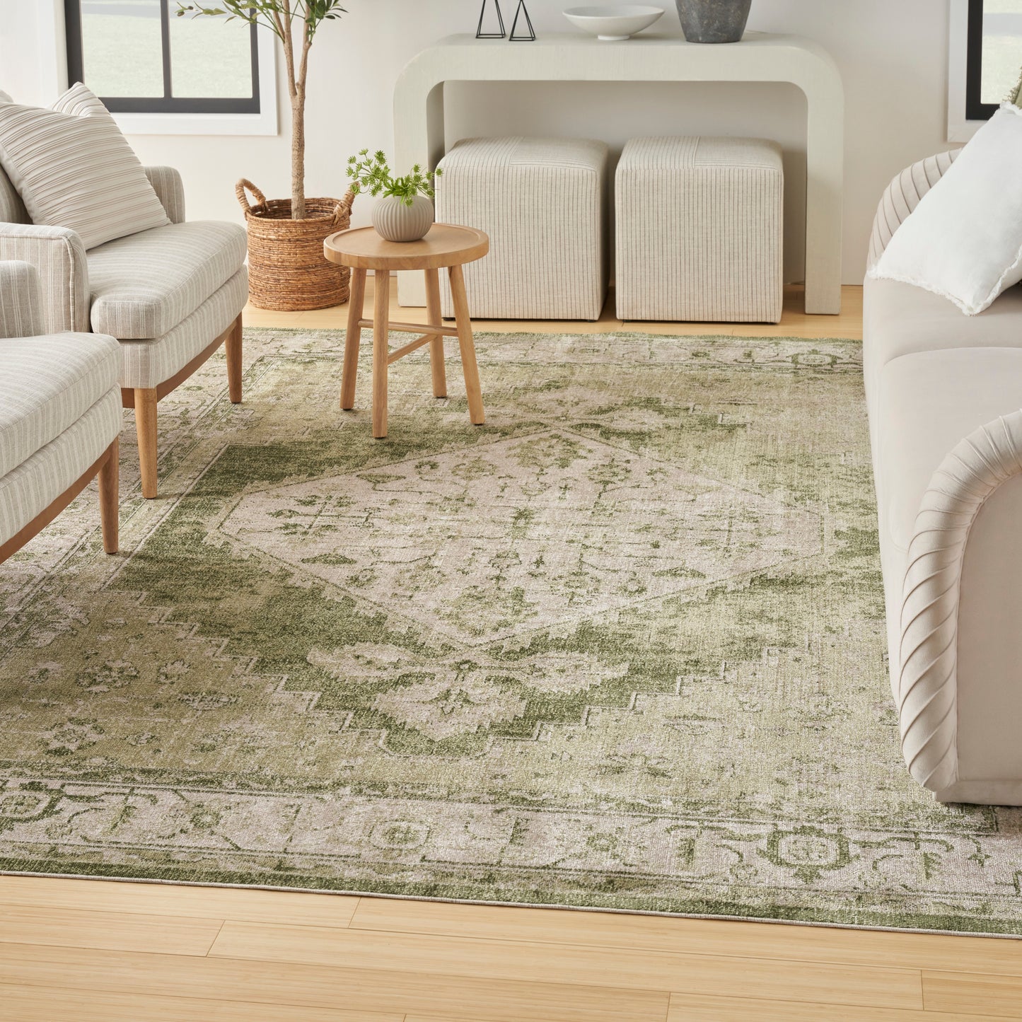 Neutral living room with olive-green patterned rug, light beige sofa and chairs, round wood table, woven ottomans.
