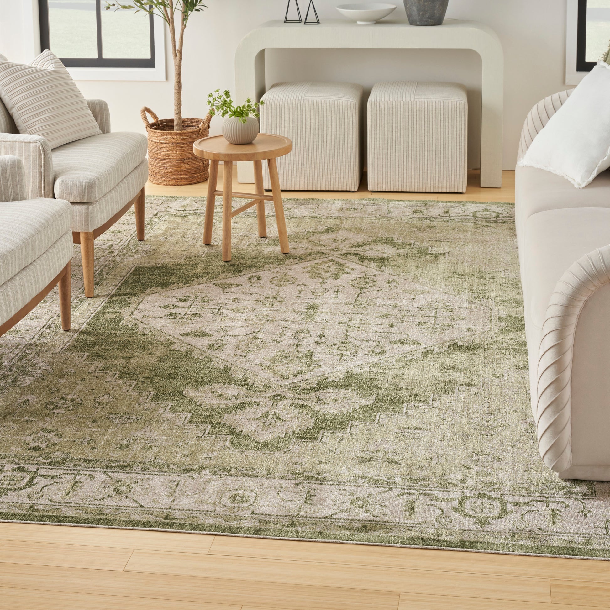 Neutral living room with olive-green patterned rug, light beige sofa and chairs, round wood table, woven ottomans.