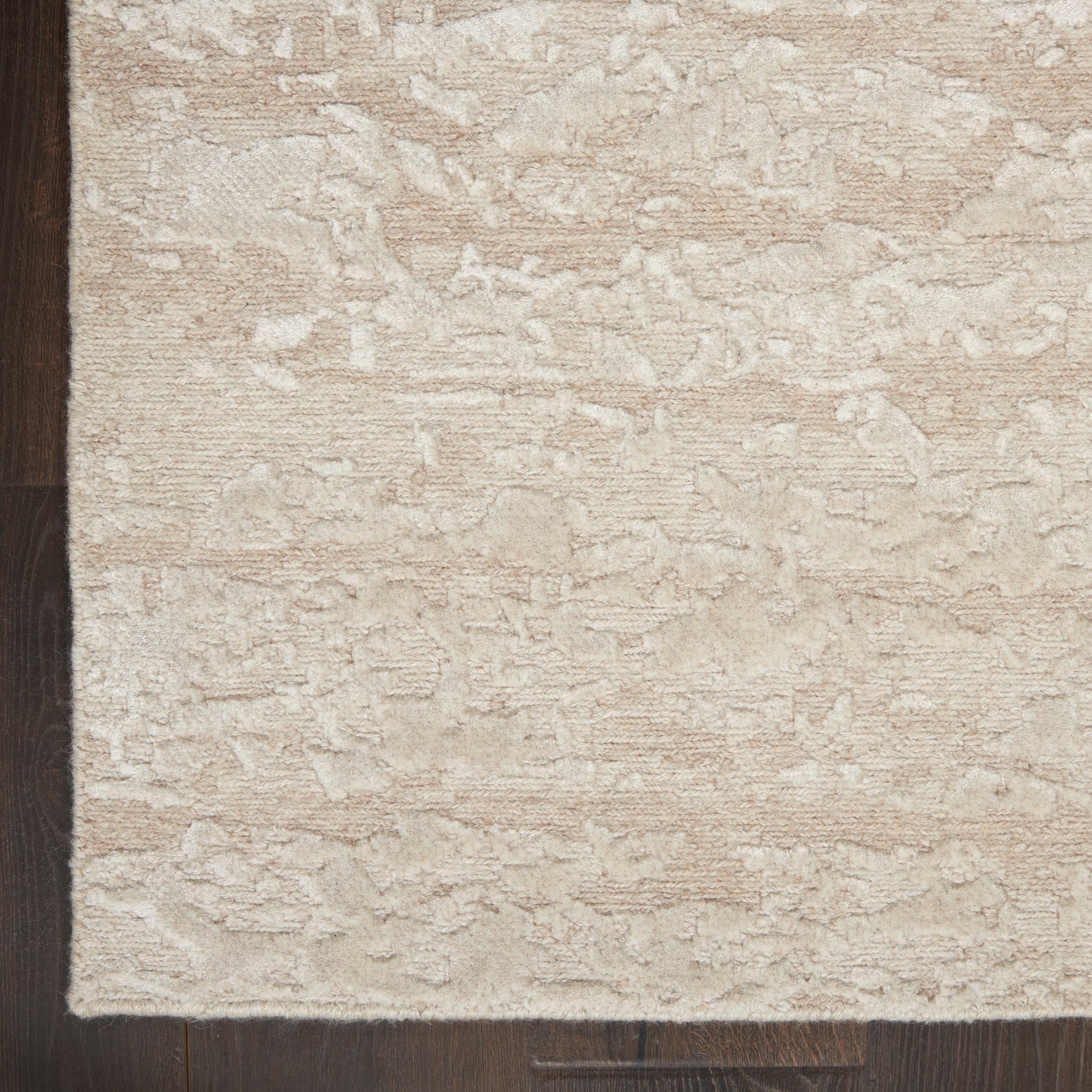 Beige textured area rug with subtle embossed pattern, plush pile, placed on dark wood flooring.