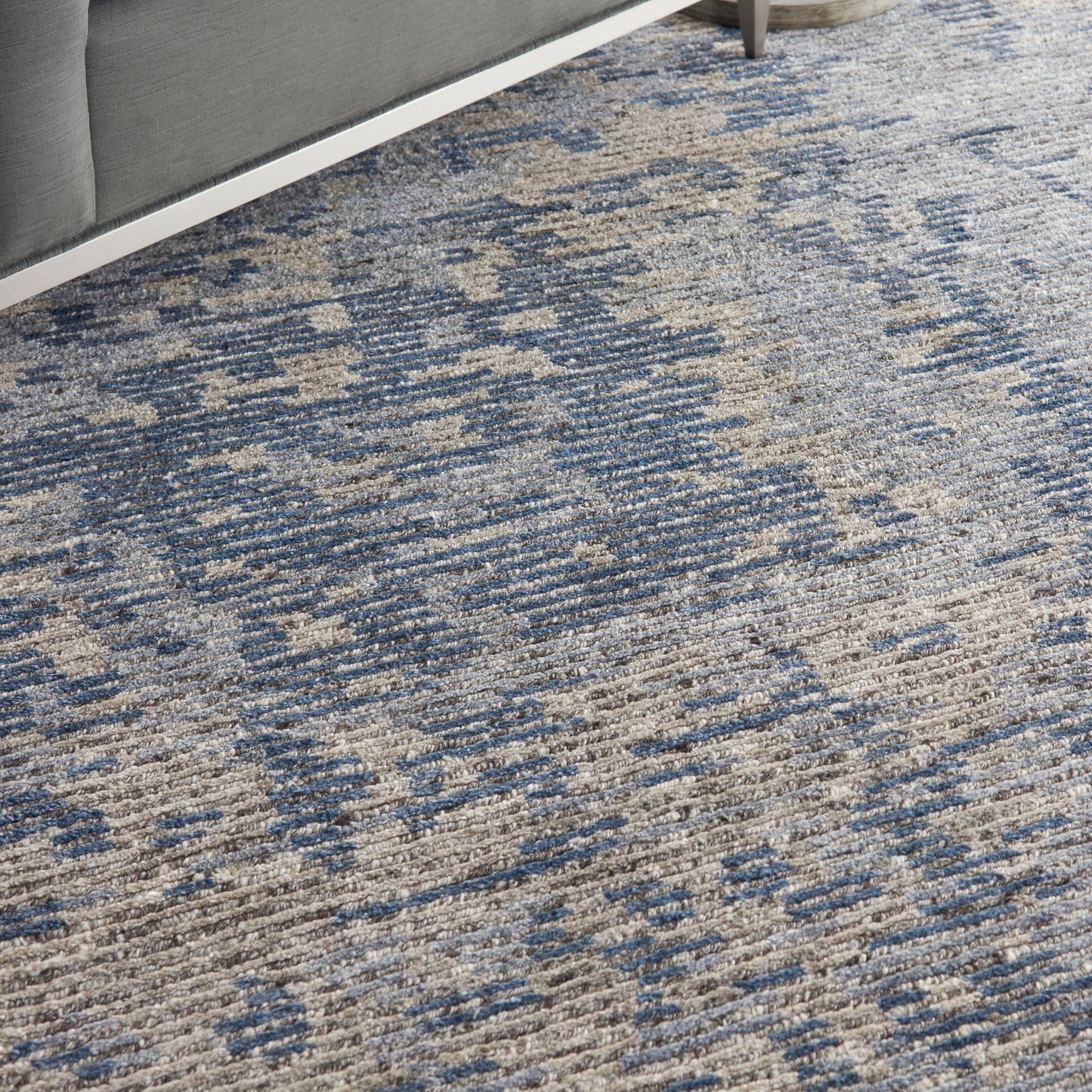 Textured blue and beige woven area rug with abstract pattern under a gray sofa.