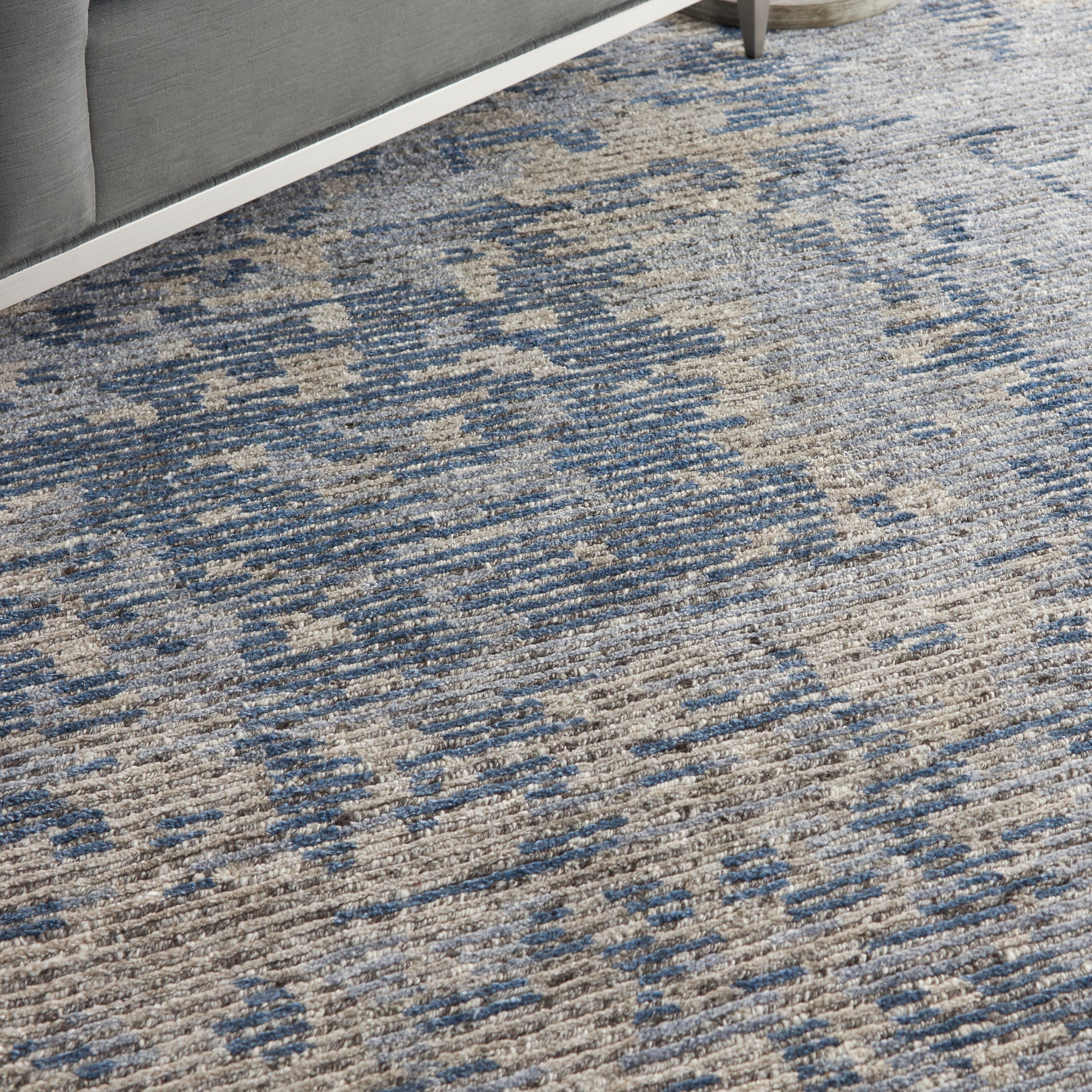 Textured blue and beige woven area rug with abstract pattern under a gray sofa.