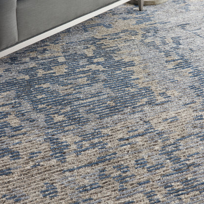 Textured blue and beige woven area rug with abstract pattern under a gray sofa.