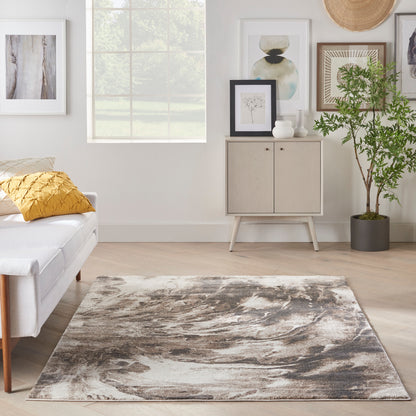 Rectangular abstract gray-beige area rug, 5' x 7', on light wood floor in a bright Scandinavian living room.