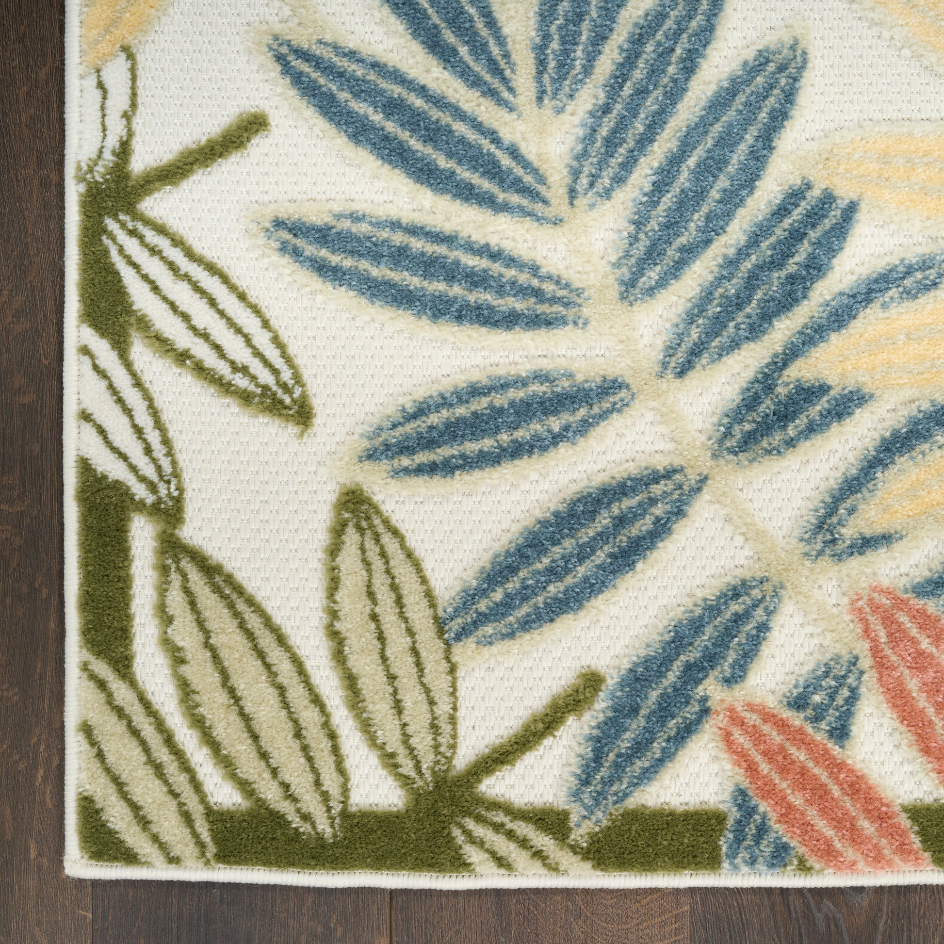 Cream rug with blue, green, yellow & coral botanical leaves; woven texture, bordered edge, on dark wood floor.