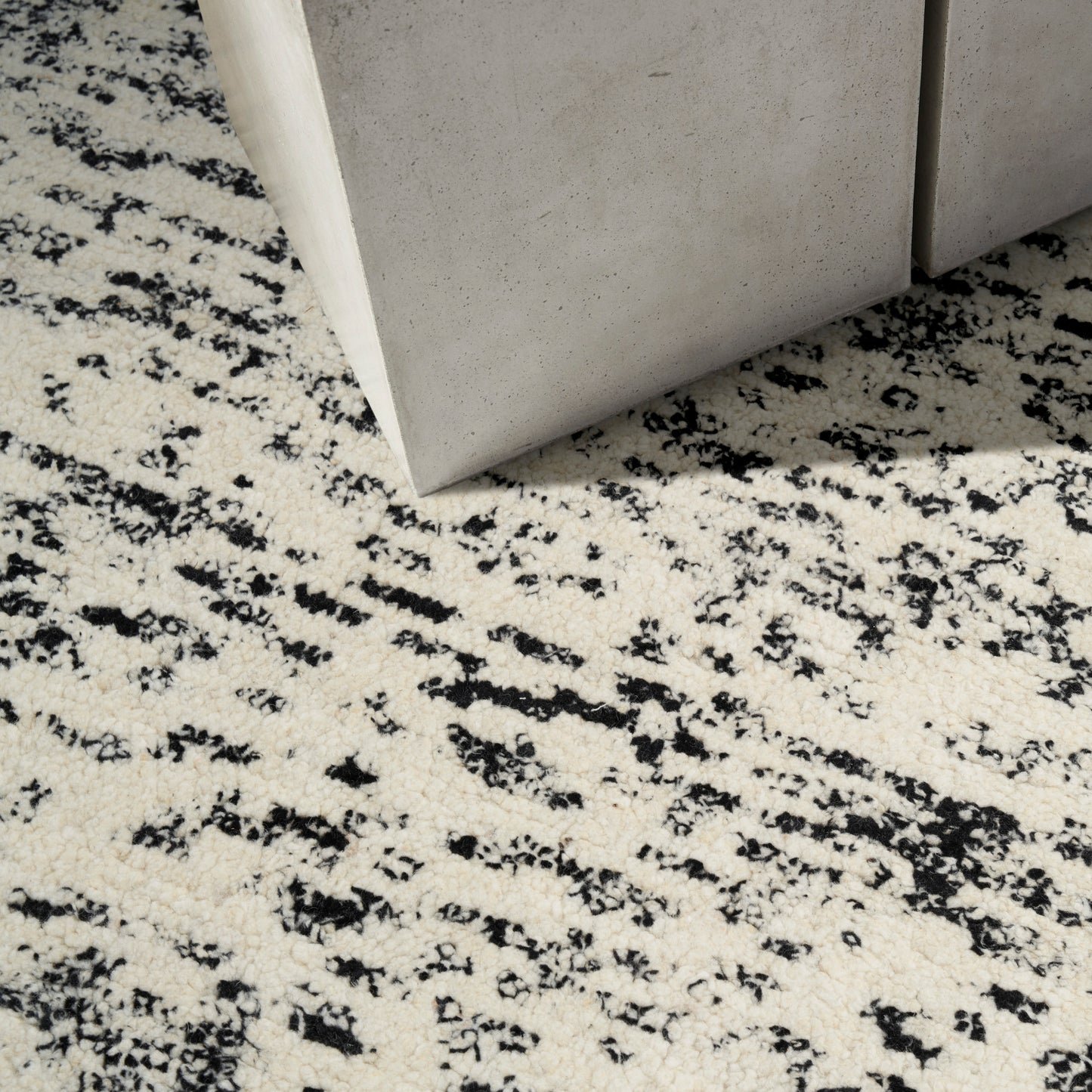 Beige speckled rug with black abstract pattern beside grey concrete blocks in a modern industrial decor setup.