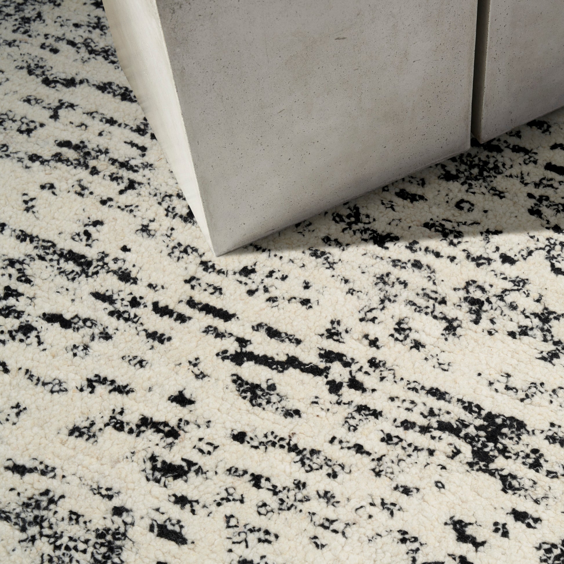 Beige speckled rug with black abstract pattern beside grey concrete blocks in a modern industrial decor setup.