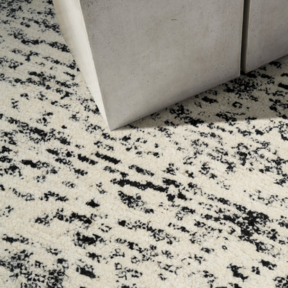Beige speckled rug with black abstract pattern beside grey concrete blocks in a modern industrial decor setup.