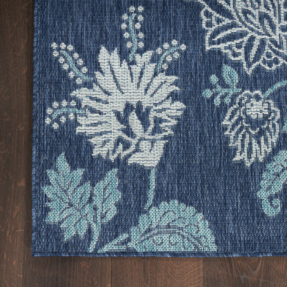 Indigo-blue woven rug with bold white floral pattern and teal leaves on dark wood floor.