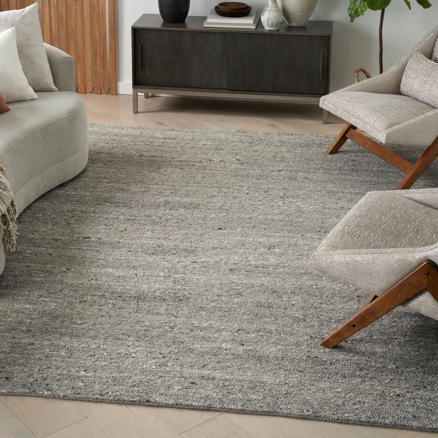 Living room with a textured gray rug, light beige sofa and wood-framed lounge chairs, and a dark wood mid-century console.