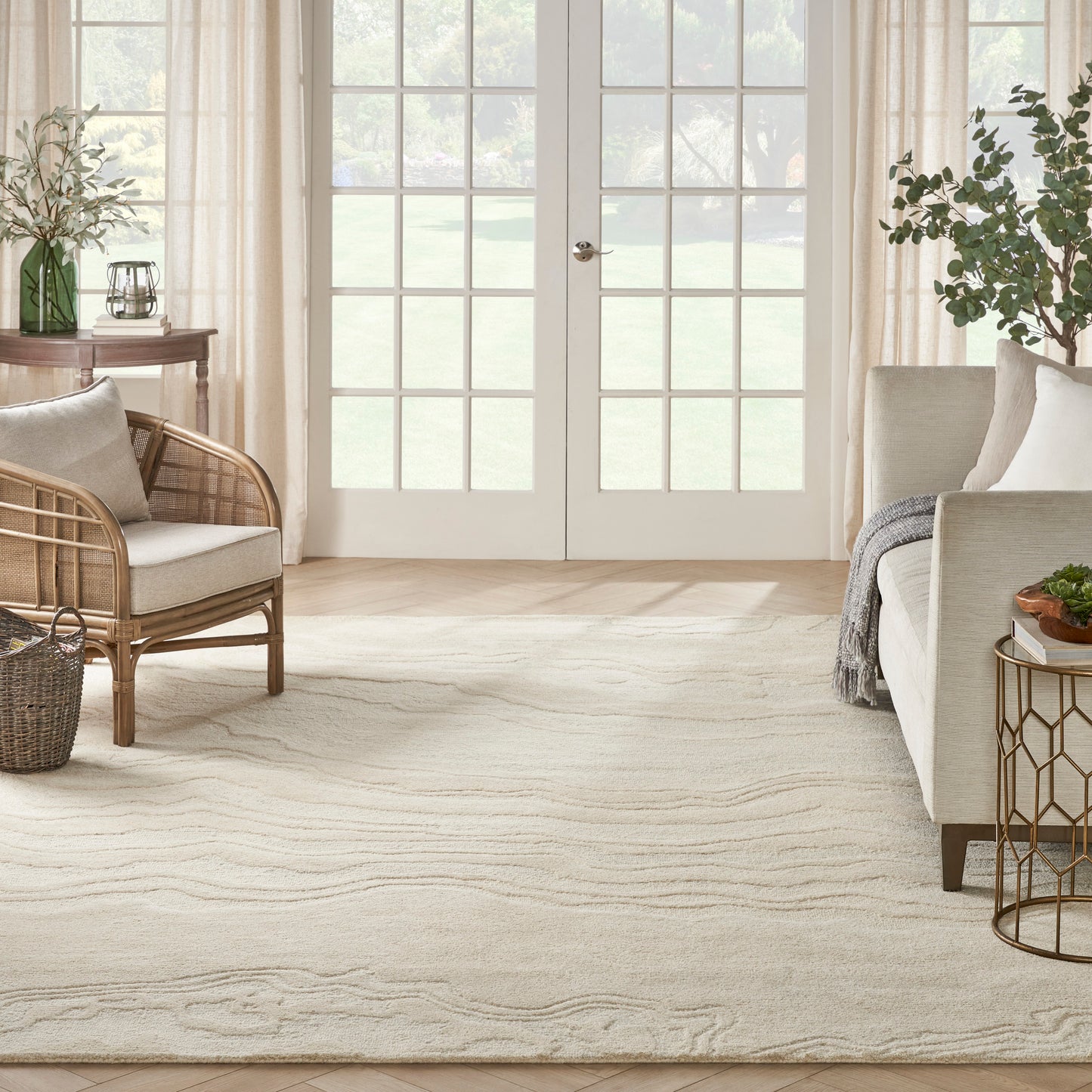 Bright living room with cream rug featuring subtle wavy pattern, wicker chair, neutral sofa, and glass French doors.