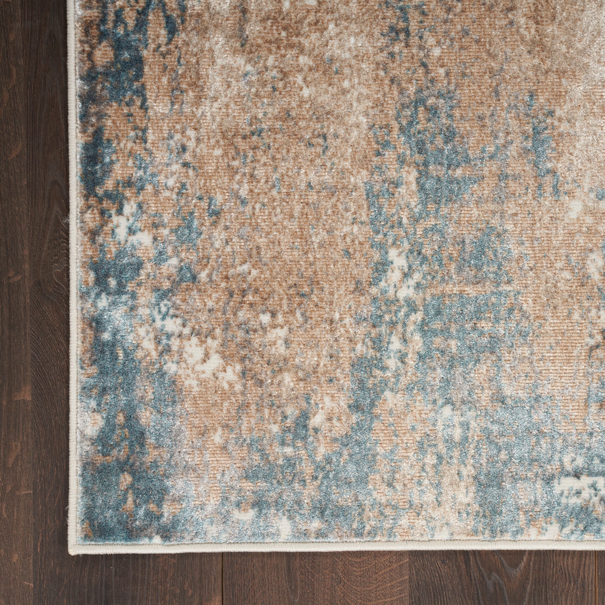 Distressed blue and beige area rug with abstract pattern and white edge on dark hardwood floor.