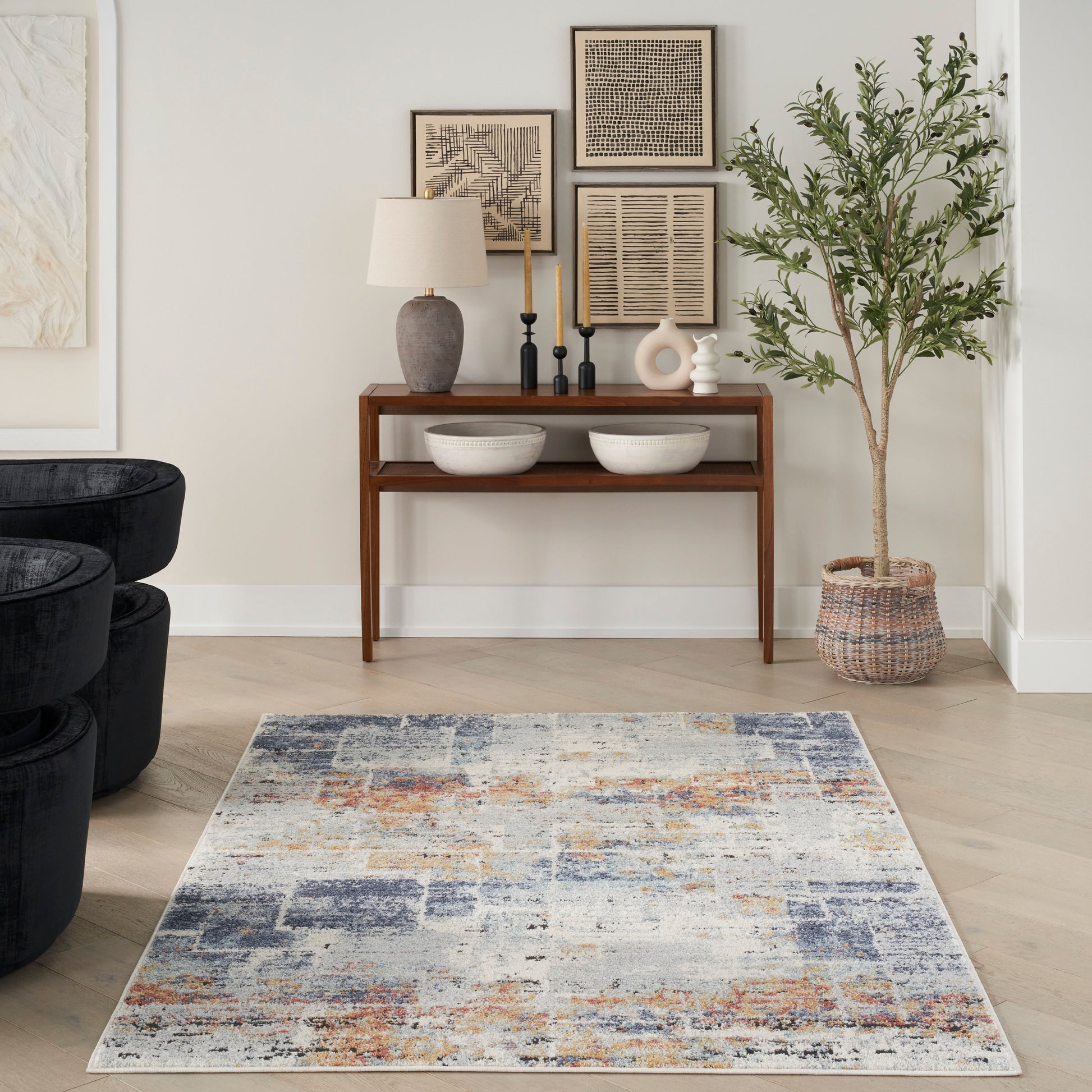 Living room with a wooden console table, framed art, lamp, two white bowls, a tall potted plant, and a blue abstract rug.