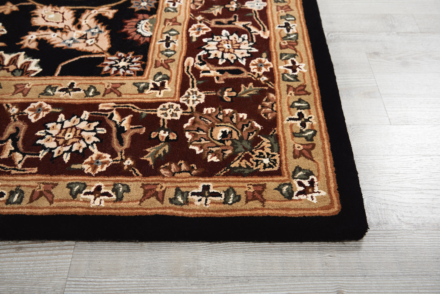 Rectangular oriental rug with dark brown field and cream-gold floral border on light wood floor.