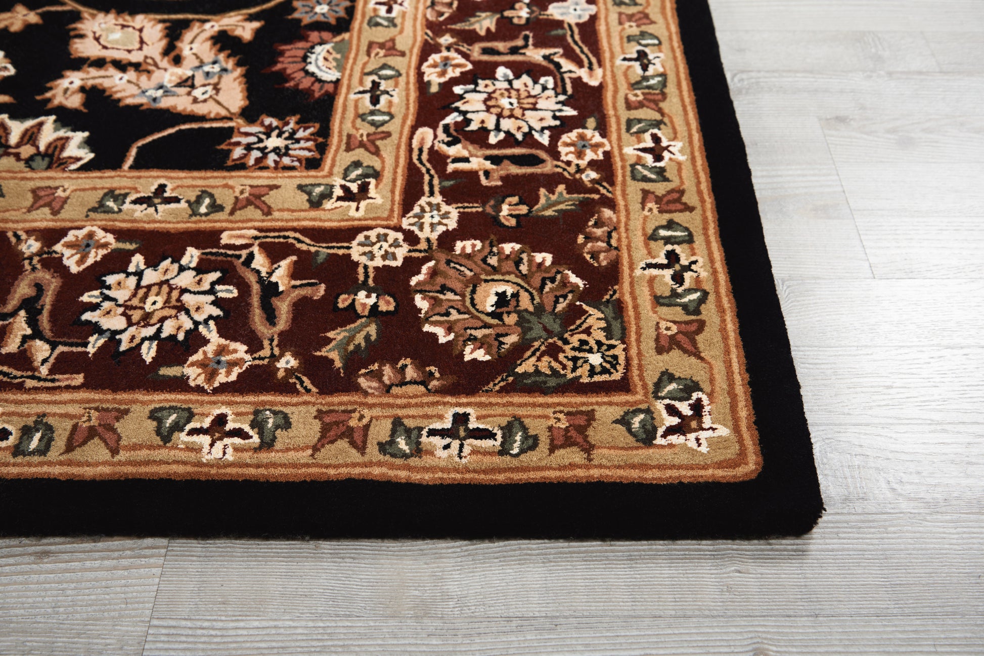 Rectangular oriental rug with dark brown field and cream-gold floral border on light wood floor.