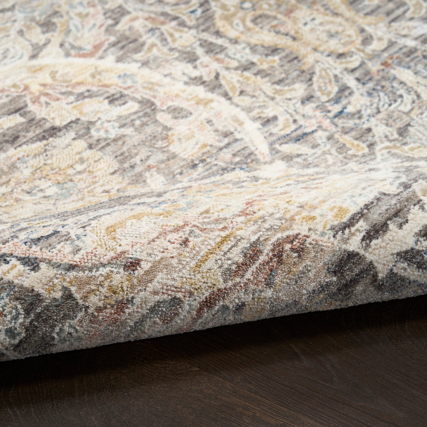 Oriental patterned area rug in cream, gray, blue & gold tones on dark wood floor; medium-pile, decorative accent.