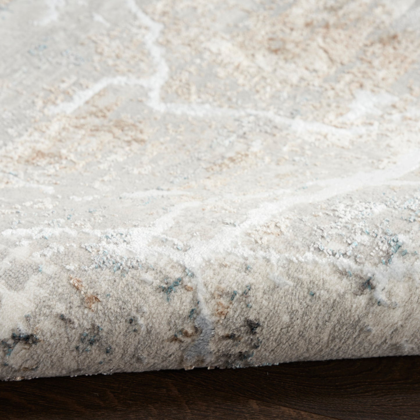 Close-up of a plush beige-gray area rug with subtle blue and tan accents and a soft textured pattern.