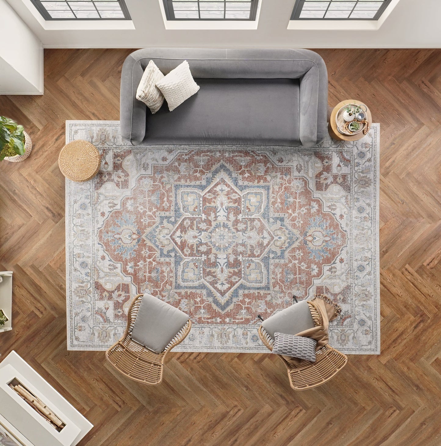 Overhead view: gray sofa, two wicker chairs & cushions, intricate blue-rust oriental rug, herringbone wood floor.