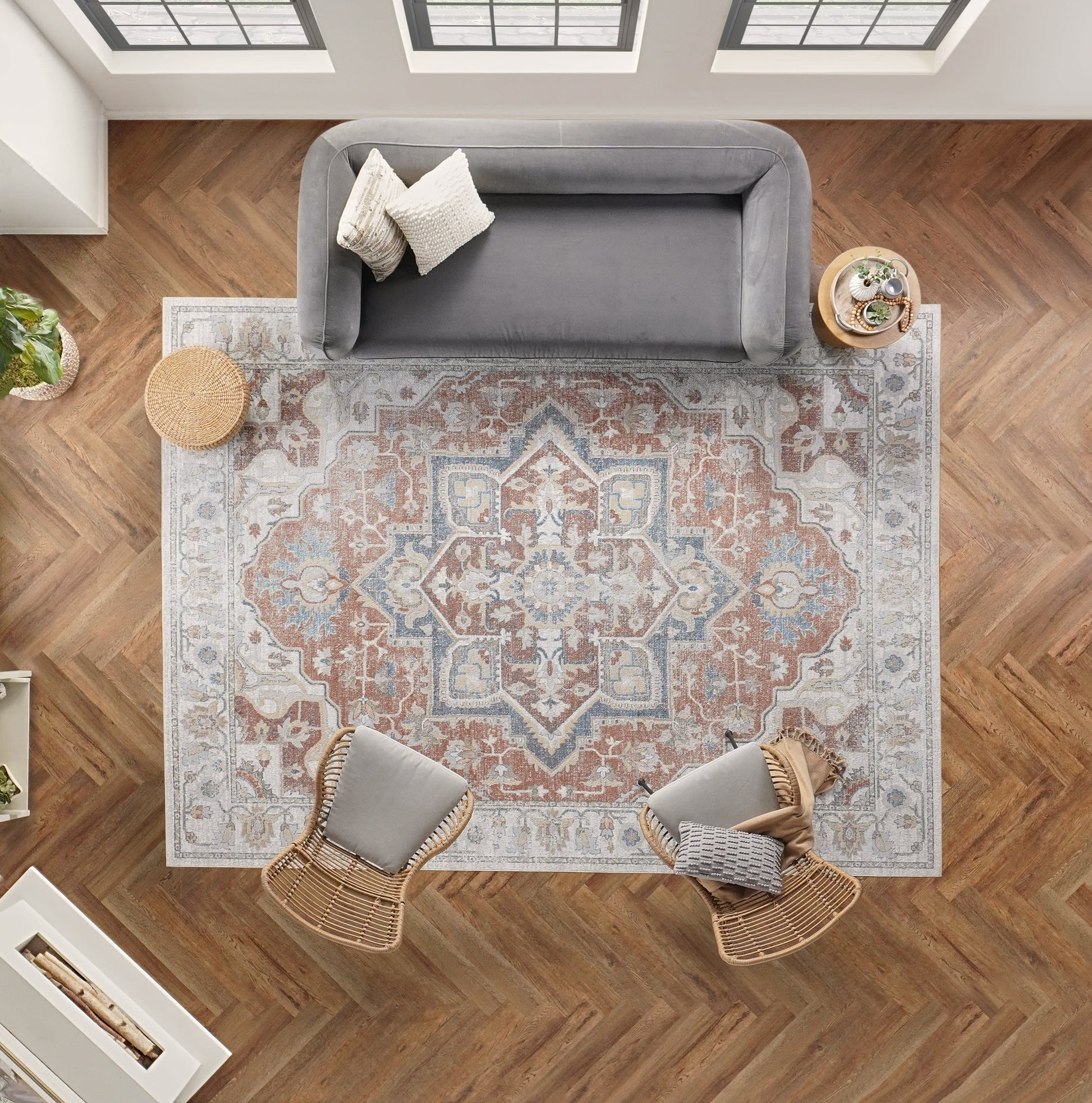 Overhead view: gray sofa, two wicker chairs & cushions, intricate blue-rust oriental rug, herringbone wood floor.