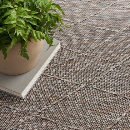 Beige ceramic pot with green fern on a hardcover book, set on a taupe woven rug with a diamond stitch pattern.