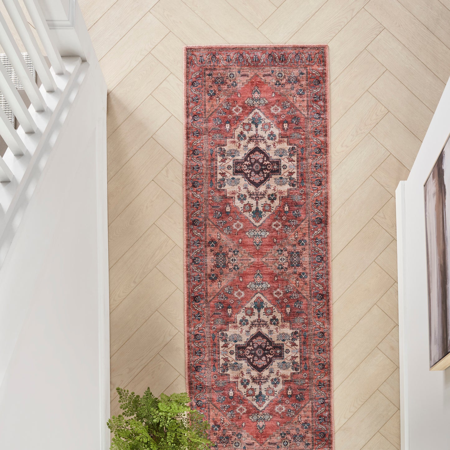Long red Persian-style runner rug with ivory and navy medallion motifs on light wood herringbone hallway floor.