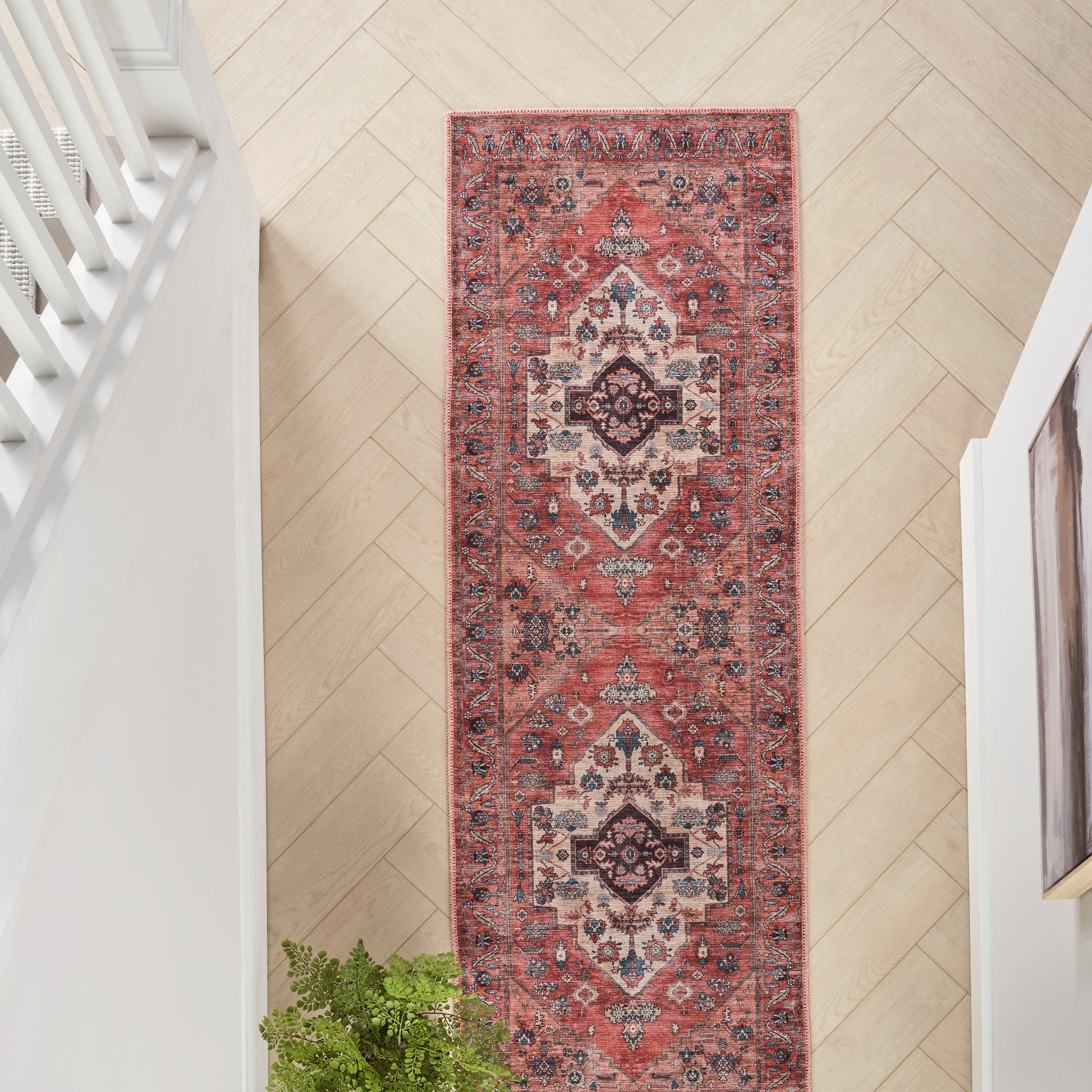 Long red Persian-style runner rug with ivory and navy medallion motifs on light wood herringbone hallway floor.