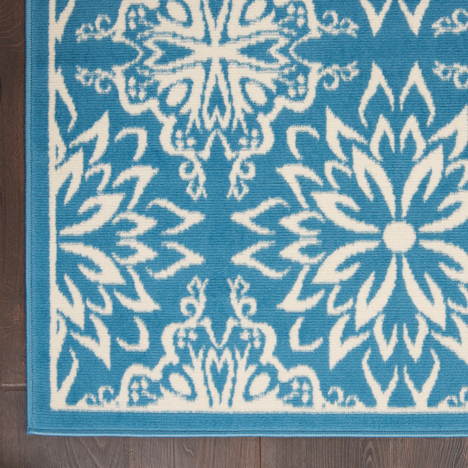Blue and white woven rug with large floral medallion motifs and turquoise border on wood floor.