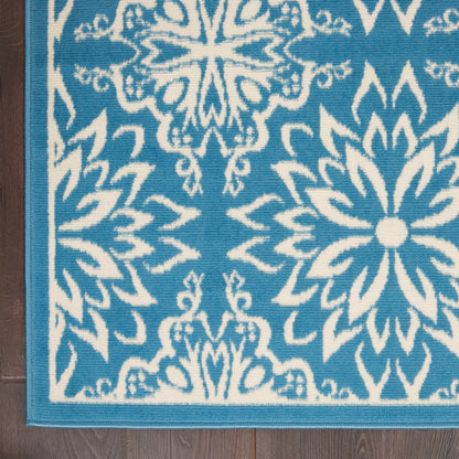 Blue and white woven rug with large floral medallion motifs and turquoise border on wood floor.