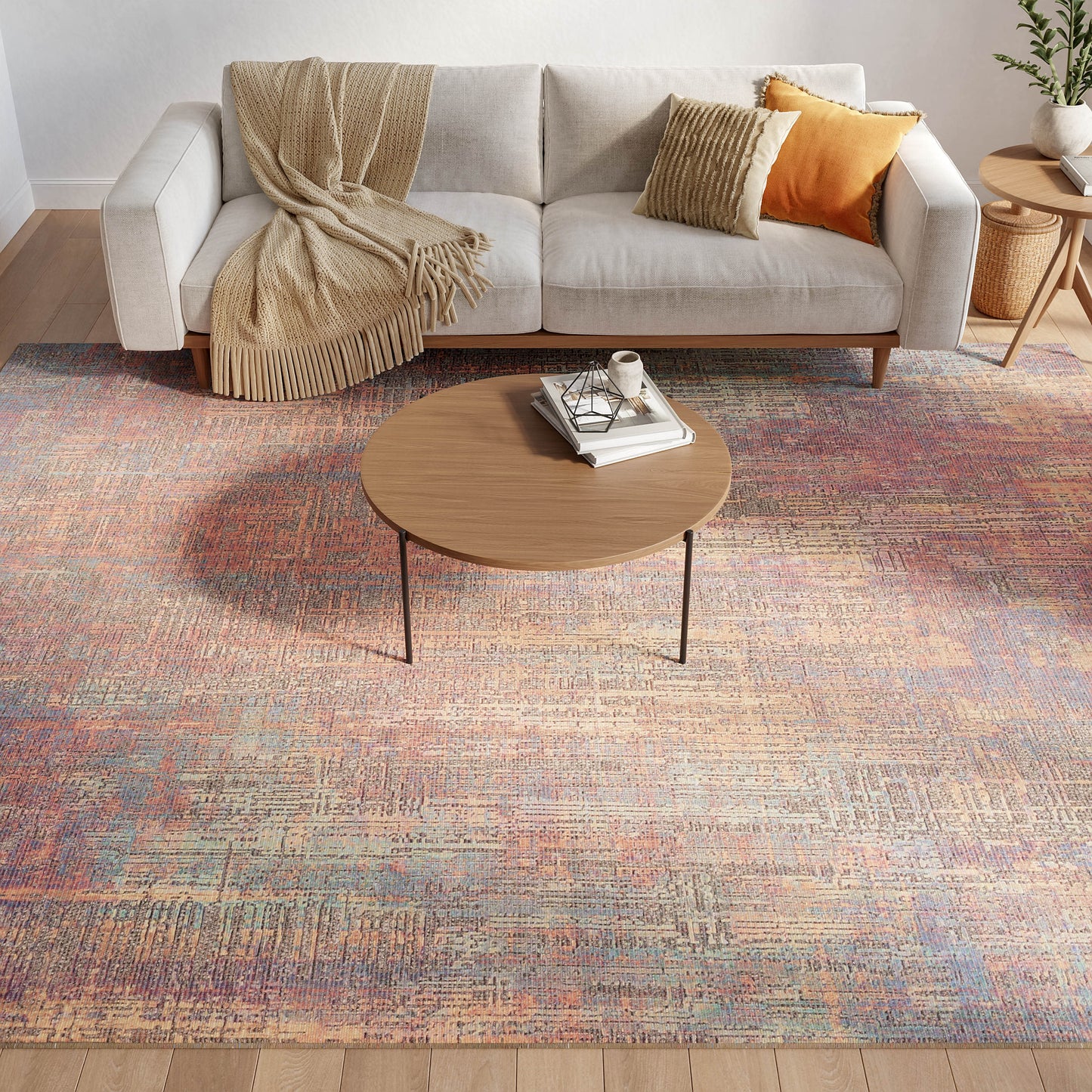 Light gray sofa with beige throw and orange and yellow cushions, wooden coffee table, colorful abstract rug, side plant.