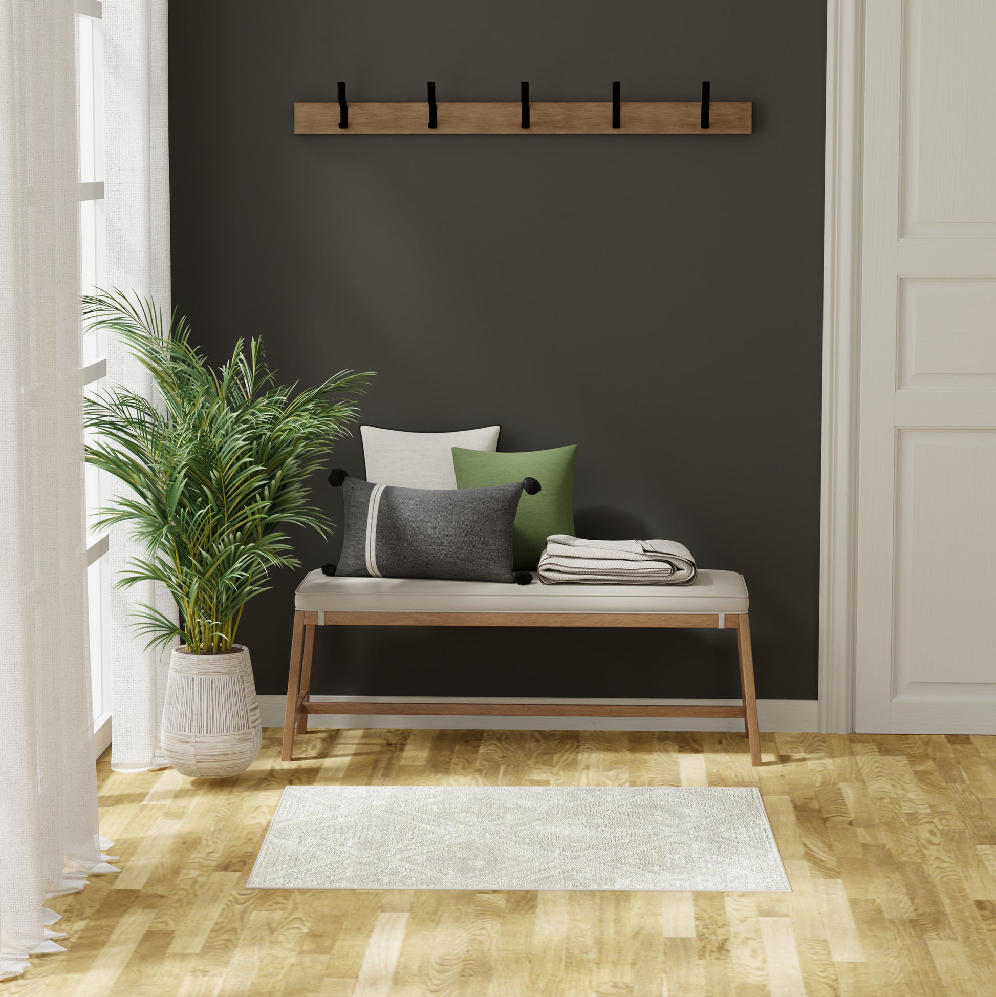 Wooden bench with beige cushion and green, gray, white pillows against a dark wall; coat rack above, potted palm beside.