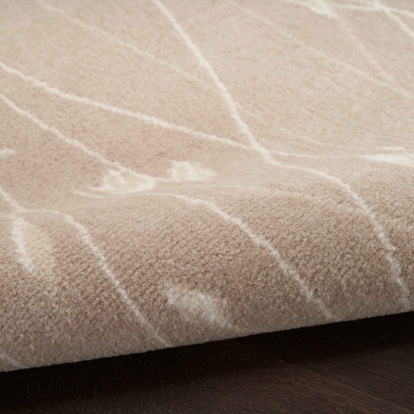 Beige plush rug with light white lines forming a subtle geometric pattern on dark wood floor.