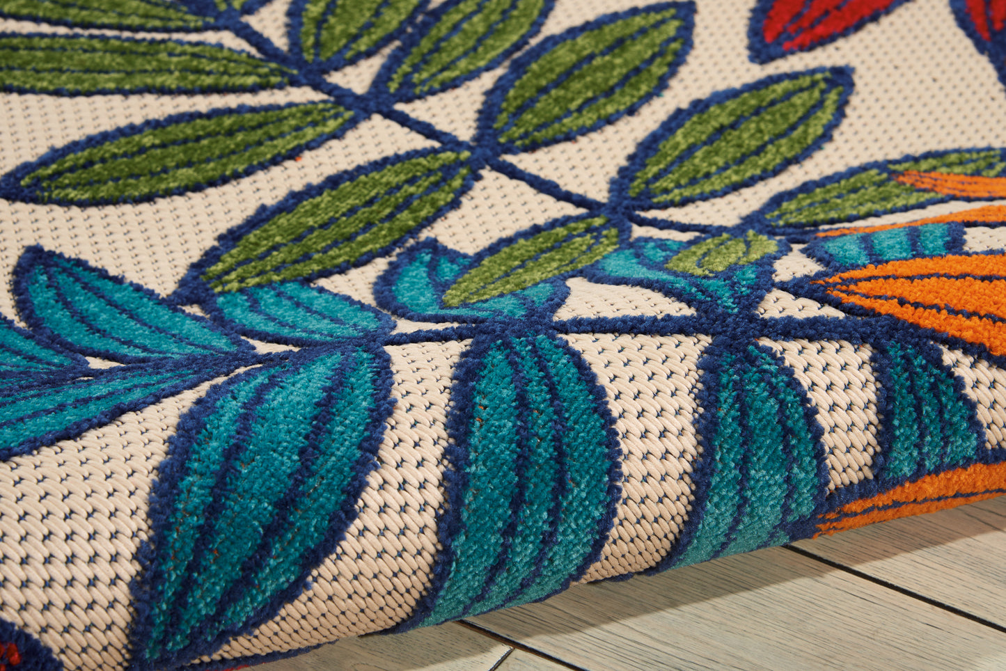 Beige woven rug with bright teal and blue leaves, green vines and orange edge accents; close-up texture.