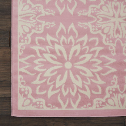 Pink rug with a large white mandala floral pattern and pale border on hardwood floor.