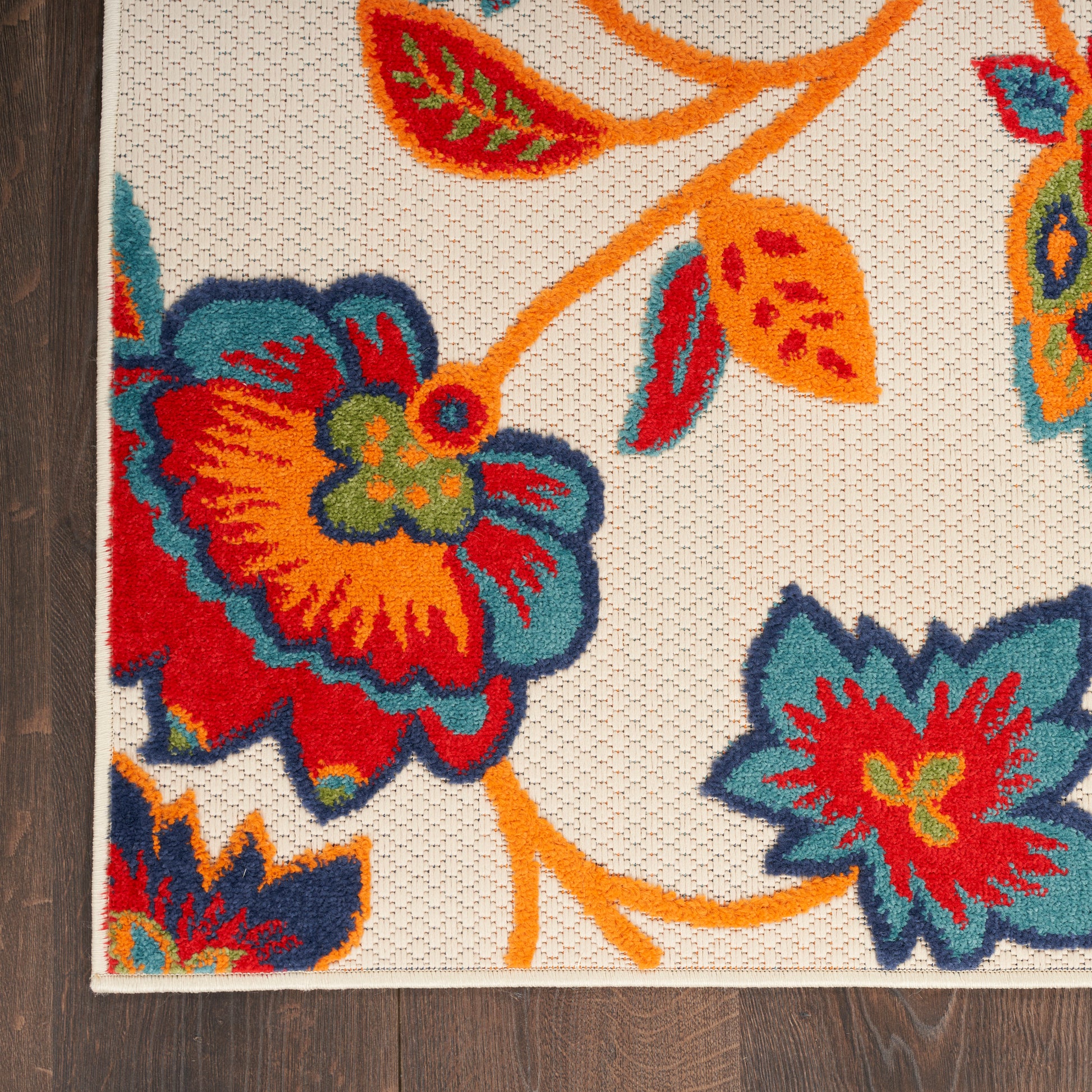 Colorful floral rug with cream background, orange stems and red, blue, teal flowers; woven texture on wood floor.