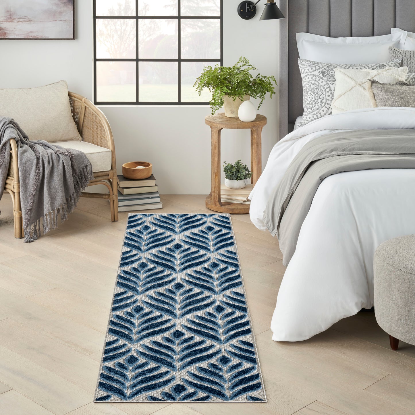 Navy blue and white leaf-patterned rug runner on light wood floor beside bed in an airy neutral bedroom.