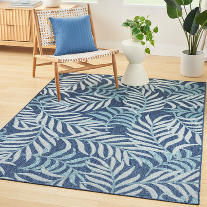 Rectangular woven area rug with navy background and teal palm leaf pattern in a bright living room.