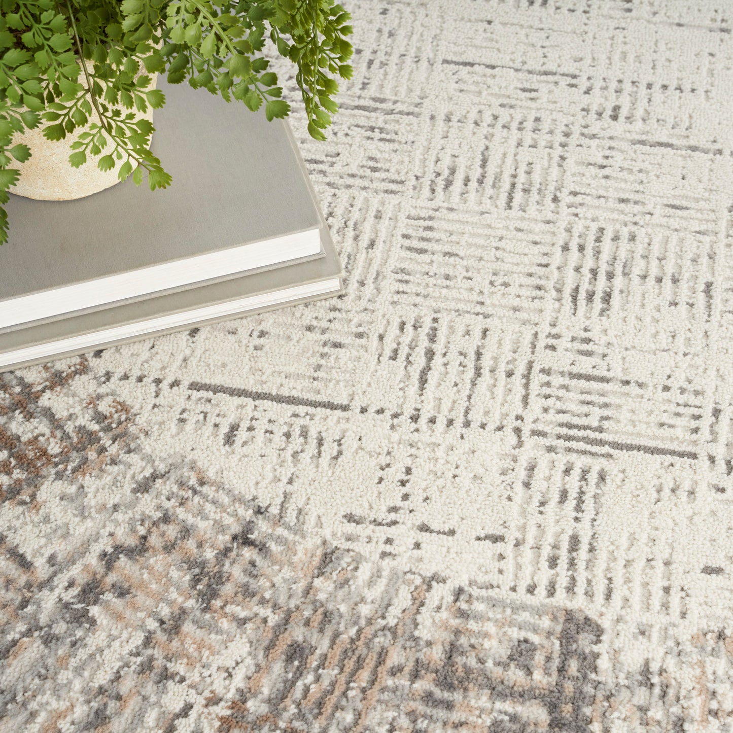 Green fern in a light ceramic pot atop a stack of books on a textured beige-gray geometric rug.