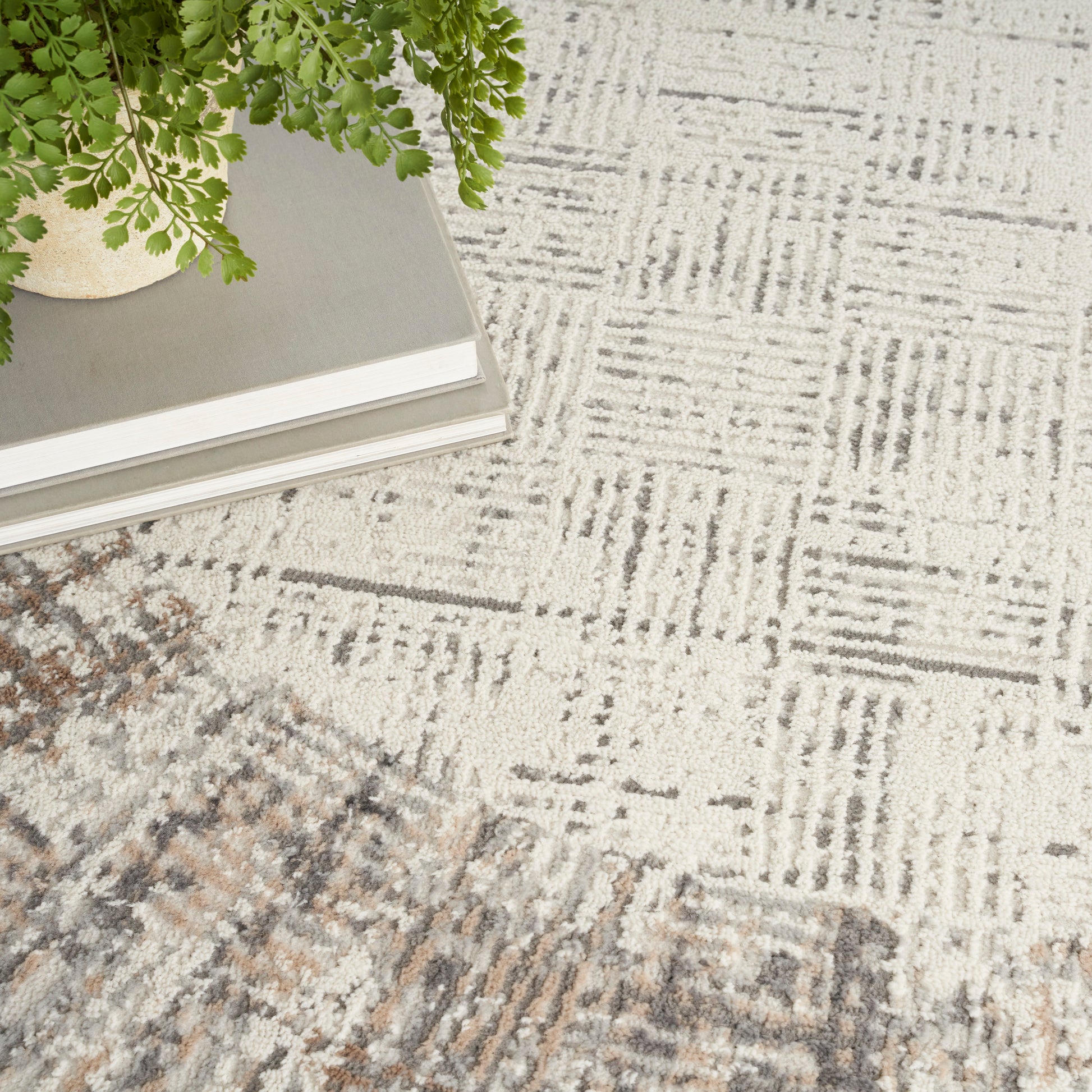 Green fern in a light ceramic pot atop a stack of books on a textured beige-gray geometric rug.