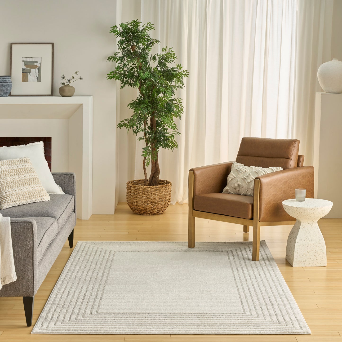 Cozy living room: gray fabric sofa, tan leather armchair, light gray geometric rug, potted plant in woven basket.