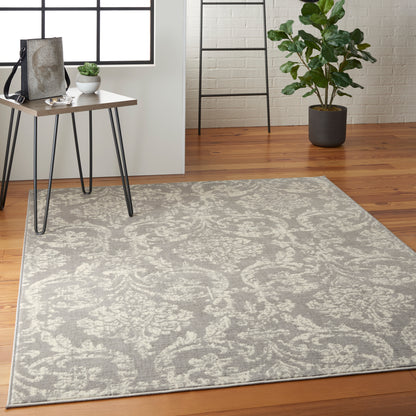 Grey damask-patterned area rug on wood floor beside a small wood table and plant, with a ladder against a white brick wall.