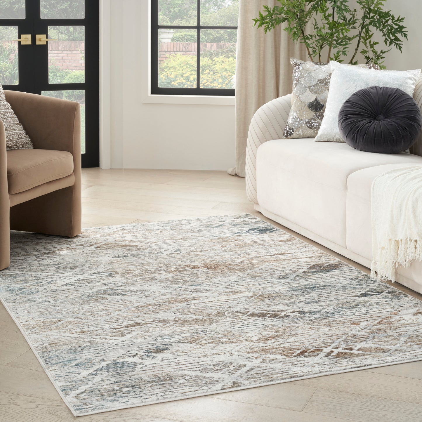 Contemporary living room with pale blue abstract rug, beige sofa with decorative pillows, brown armchair, and plant.
