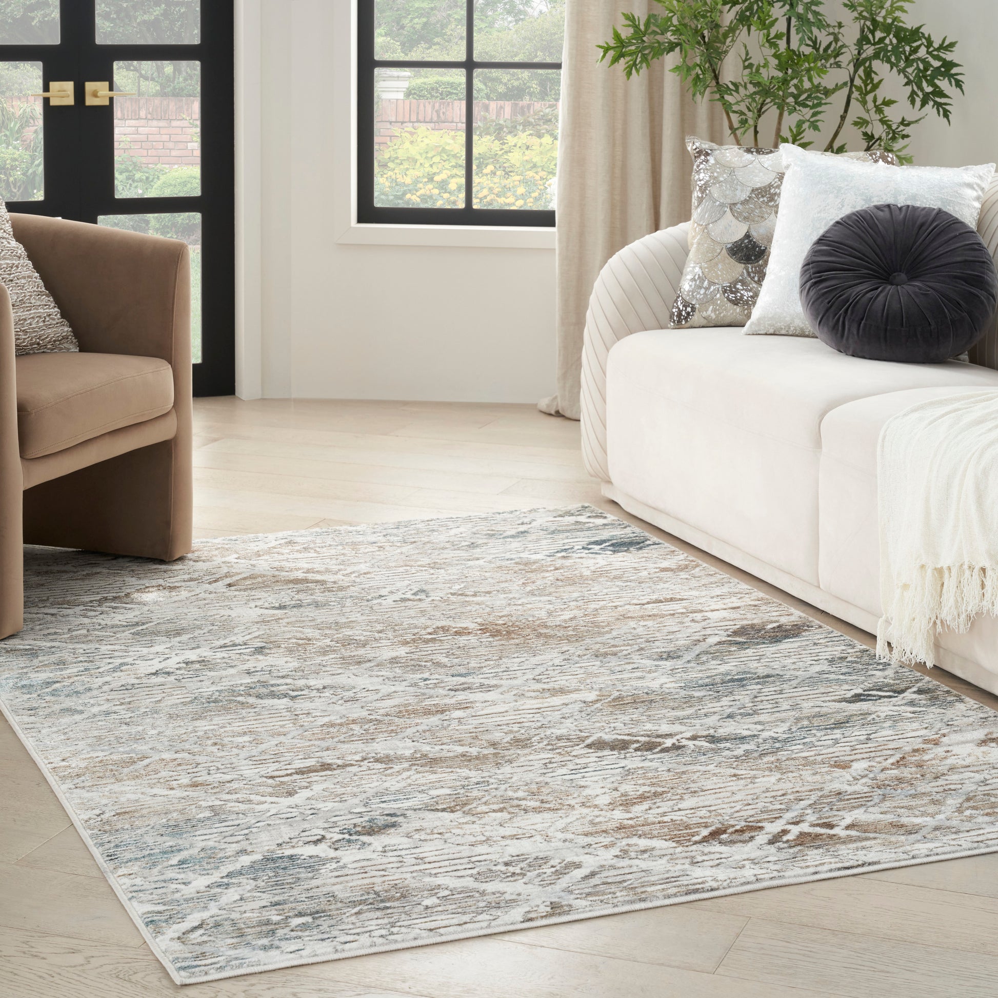 Contemporary living room with pale blue abstract rug, beige sofa with decorative pillows, brown armchair, and plant.
