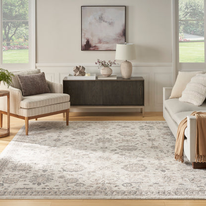 Neutral living room with a beige armchair, gray sofa, dark wood credenza, abstract art, ceramic lamp, and a patterned rug.