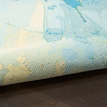 Pastel blue, teal, and cream woven rug with abstract watercolor pattern, rolled edge on dark wooden floor.