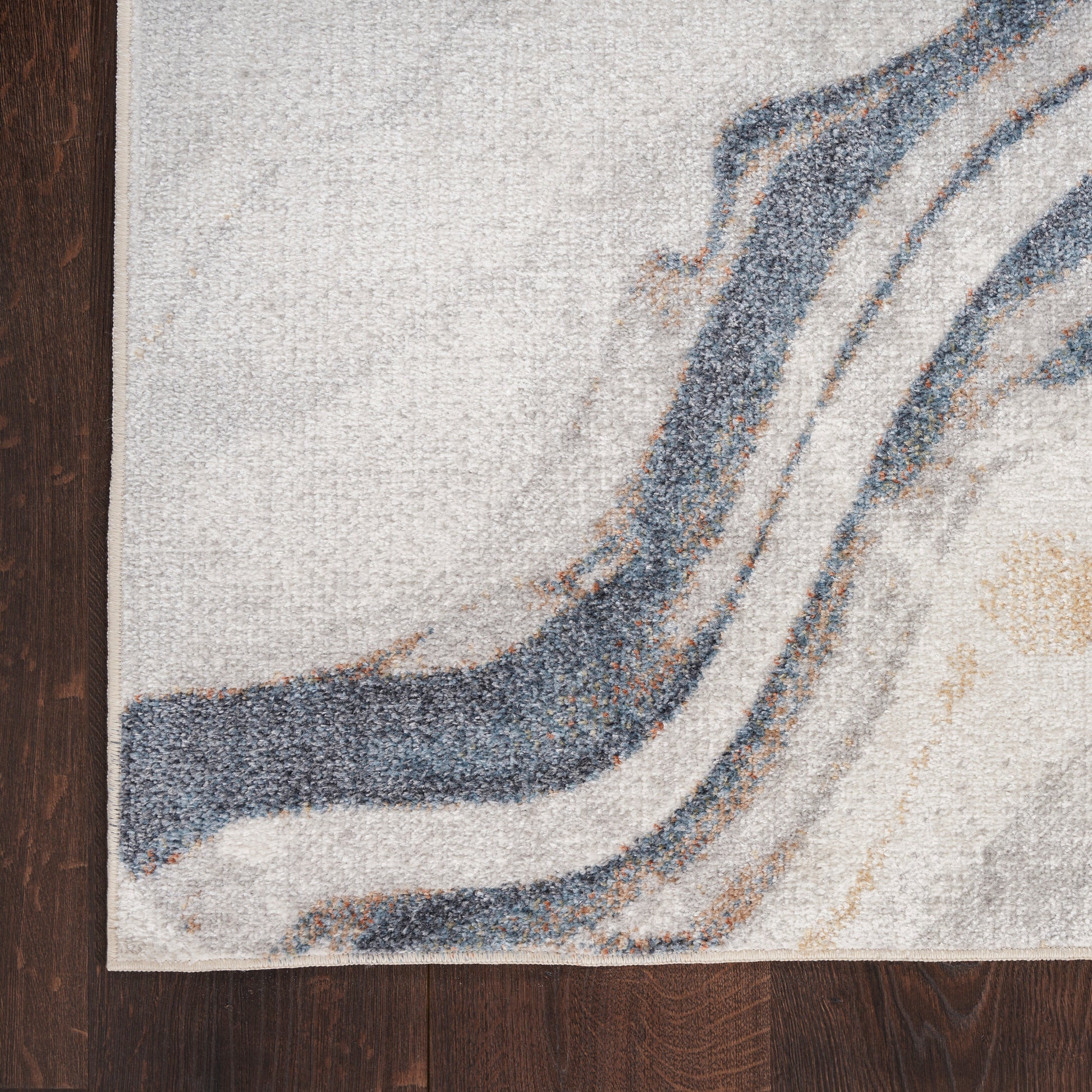 Abstract-patterned area rug with blue-gray curved lines on a beige background, laid on dark wood flooring.