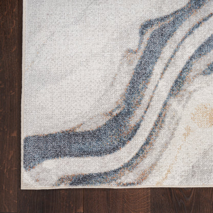 Abstract-patterned area rug with blue-gray curved lines on a beige background, laid on dark wood flooring.
