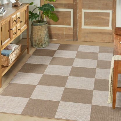 Beige and taupe checkered rug with large squares in a cozy entryway beside a wooden sideboard and wicker baskets.