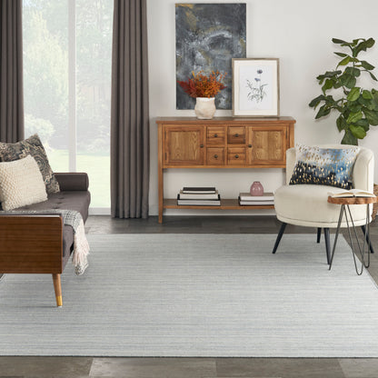 Mid-century teak sideboard with framed art, vase of orange flowers, plant, cream accent chair, sofa with cushions, and gray rug by a large window.