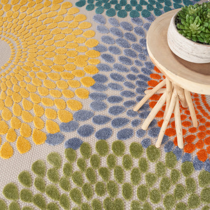 Multicolor sunburst round rug (8' diameter) with yellow, blue, green, and orange petal motifs; a small round wooden table with a potted succulent visible beside it.