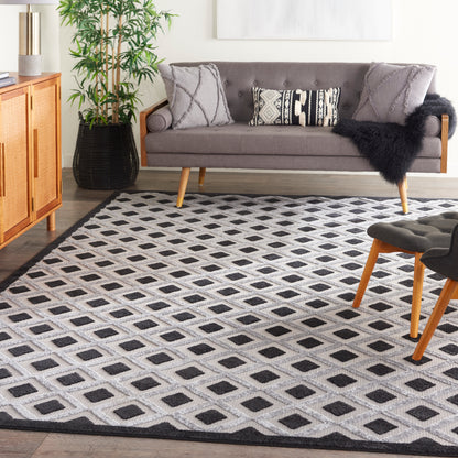 Living room with mid-century gray sofa, black-and-white diamond rug, wooden cabinet, potted plant & light-wood legs.